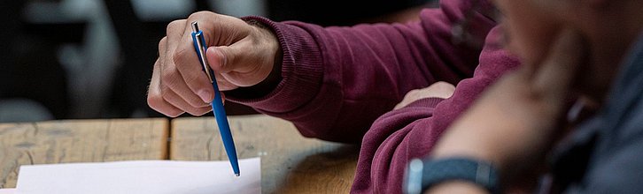 Hände mit Stift und Papier in einer Beratungssituation.
