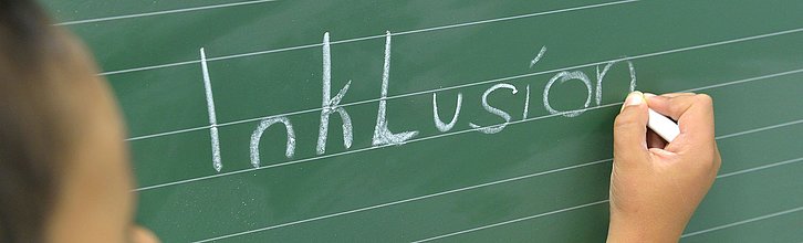 Kind schreibt das Wort Inklusion auf eine Tafel
