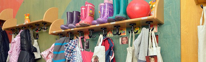 Garderobe in einer Kita; zu sehen sind Gummistiefel, Jacken und Bilder von Kindern